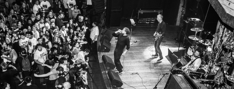 Banda Black Flag tocando para plateia cheia em foto preto e branca