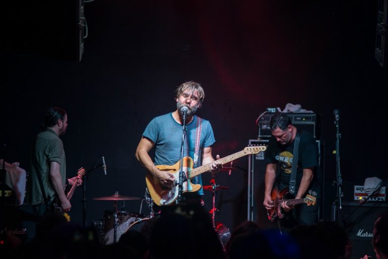 Banda Mineral se apresenta em palco escuro visto por pessoas