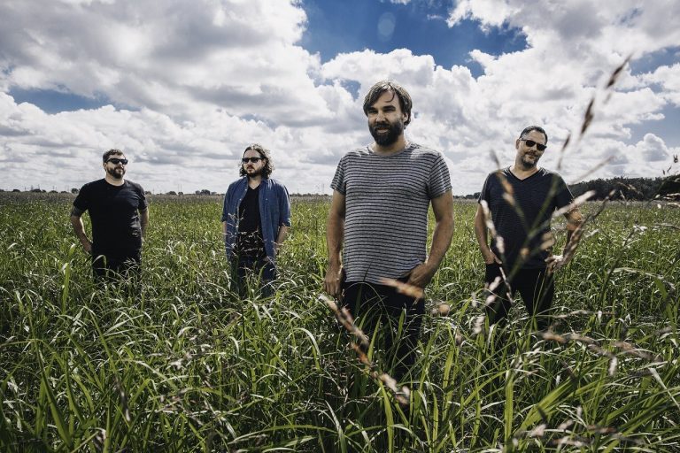 Banda Mineral tira foto em campo verde com ceu azul enevoado atrás