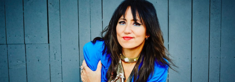 A cantora KT Tunstall sorri para foto de camisa azul e fundo cinza